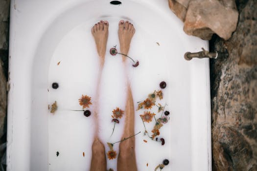 Top view of a woman's bare legs in a bathtub filled with milk and scattered flowers for a soothing bath experience.